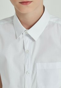 Chemise col blanc avec une poche avant, fabriquée en tissu lisse ; possède un design à boutons et une texture uniforme.