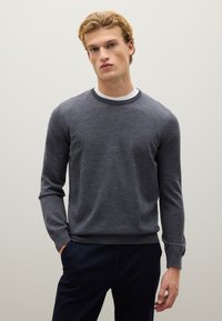 Maglione grigio a maniche lunghe con scollo a girocollo. Tessuto morbido, polsini e orlo a coste, abbinato a una maglietta bianca sotto. Design semplice.