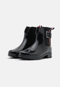 Bottines noires en vernis avec des panneaux latéraux élastiques, un accent de boucle sur le côté et une semelle en caoutchouc texturée pour une bonne adhérence.