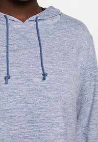 Hellblaues Hoodie aus strukturiertem, meliertem Stoff. Verfügt über eine Kordelzugkapuze und eine lockere Passform. Enthält eine Kängurutasche.