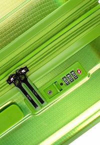 Valigia rigida verde con superficie testurizzata, doppia cerniera nera, serratura a combinazione e dettagli lisci in diverse tonalità di verde.