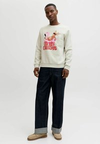 Lichtgrijze sweatshirt met de tekst "VROLIJK KERSTFEEST" en een roze flamingo en rendier, gecombineerd met donkerdenim jeans en beige instappers.