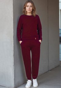 Felpa bordeaux e pantaloni jogger abbinati in morbido tessuto, con un design aderente, polsini a costine e tasche, abbinati a sneakers bianche.