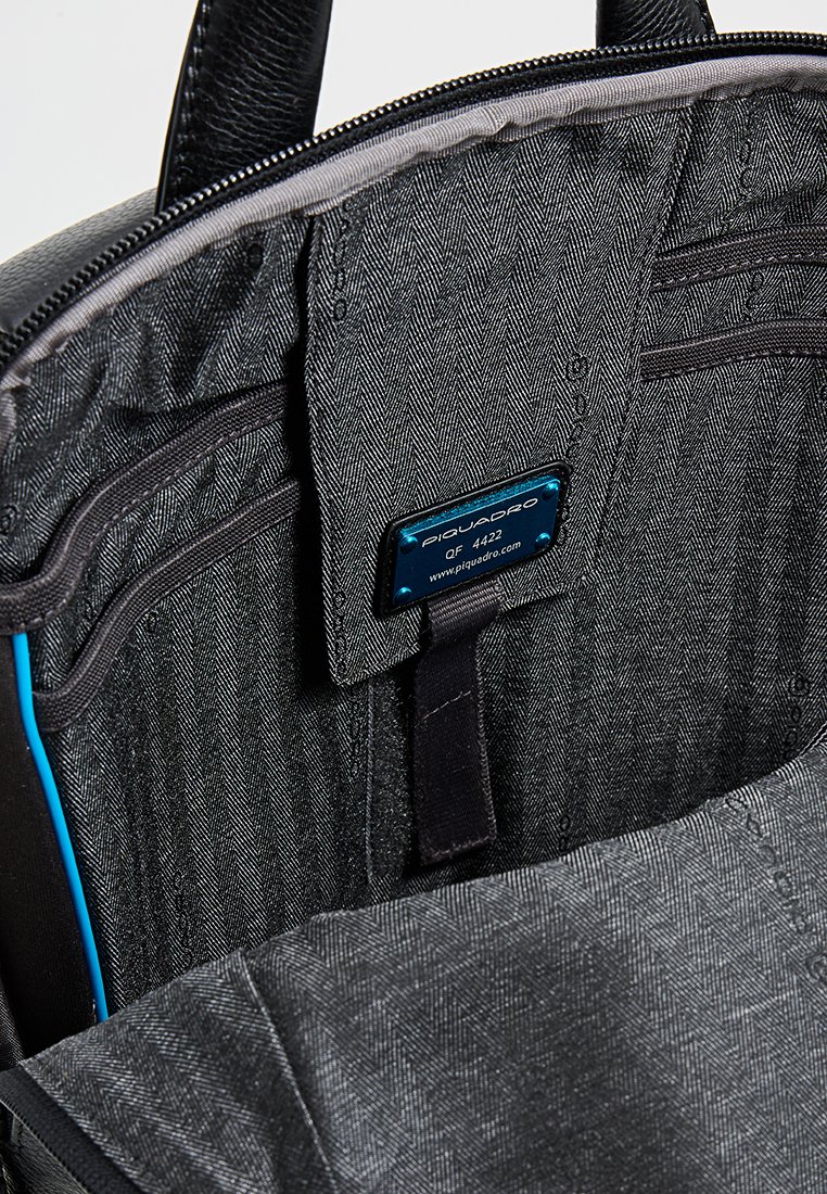 Zwarte rugzakinterieur met een visgraatstructuur. Voorzien van ritszakken, elastische banden en een blauw label. Zachte stofvoering.