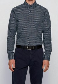 Langarm overhemd met knopen in donkere stof met een diamantpatroon in het blauw. Gecombineerd met donkere broek en een zwarte riem.