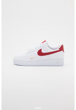 Niski biały sneaker z czerwonym logo Nike, czerwoną zakładką na pięcie i złotym akcentem po boku, pokazany na jednolitym jasnym tle.