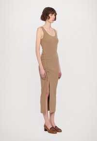 Knit brown midi-mekko, jossa on pyöreä kaula-aukko, säädettävä sivurypytys ja reiden halkio. Yhdistetty ruskeisiin korkokenkiin, joissa on teksturoitu yksityiskohta.