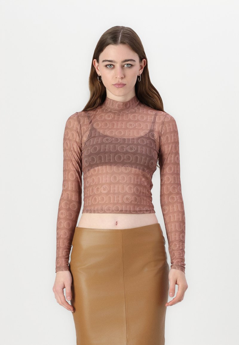 Hnědý dlouhý rukávový crop top z průhledné látky s opakovaným logem "HUGO". V kombinaci s hnědou koženou sukní s vysokým pasem.