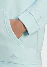 Sweat à capuche bleu clair avec une finition texturée, doté d'une poche kangourou et d'un détail en relief "ALL SZN" sur le poignet, ainsi que le logo Adidas.