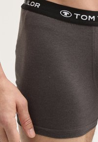 Graue Baumwollboxershorts mit einem schwarzen elastischen Bund, der das weiße Logo "TOM TAILOR" trägt. Der Stoff wirkt glatt mit minimaler Textur.
