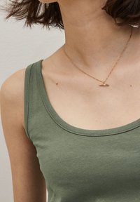 Débardeur vert olive avec un col rond, fabriqué dans un matériau doux et texturé. Présente un collier délicat avec une barre dorée en accent.