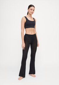 Schwarzes Sportset bestehend aus einem enganliegenden Crop-Top und weiten Leggings. Der Stoff ist glatt mit einem leichten Glanz und sorgt für Komfort und Flexibilität.