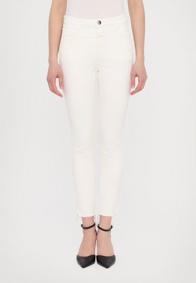 Jeans skinny blancs à taille haute, avec un design de poche avant et un ourlet effiloché. Associés à des talons noirs à bout pointu.