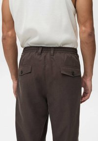Braune Baumwollhosen mit elastischem Bund und zwei Gesäßtaschen, die mit Knöpfen geschlossen werden. Glatte Textur, lockere Passform.