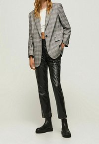 Blazer de cuadros gris de gran tamaño sobre una camiseta blanca corta, combinado con pantalones de cuero negros y botines negros, textura suave y diseño estructurado.