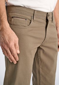 Pantalones caquis hechos de una tela texturada, con un bolsillo lateral con un acento a rayas, botones de metal y una cintura ajustada.