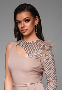 Mouwloze jurk in zacht beige met een gestructureerd mesh off-shoulder detail en veeraccenten. Heeft een aansluitende silhouet met een uitsnijdingen ontwerp.