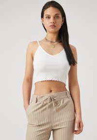 Witte geribde crop top met een gegolfde onderrand, gecombineerd met beige gestreepte broek met een elastische tailleband en trekkoord voor aanpassing.