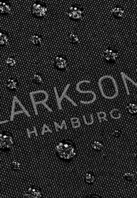 Gocce d'acqua che si formano su un tessuto scuro e texturizzato con testo parzialmente visibile "HARKSON HAMBURG."