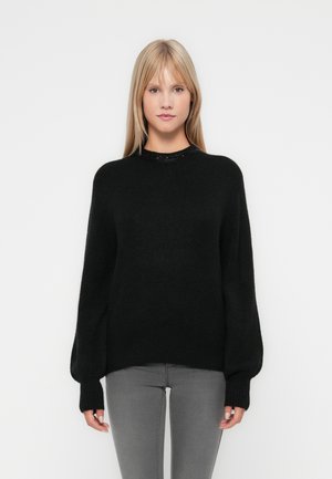 Black knitted sweater with a round neckline, wide sleeves, and ribbed cuffs. Worn over gray jeans, featuring a smooth texture and relaxed fit.