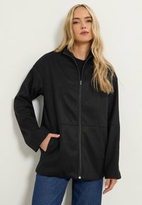 Svart zip-up-jacka i mjukt tyg med krage, sidofickor och avslappnad passform. Har minimala sömmar och inga synliga mönster.