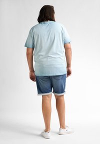 Lys blå bomulds t-shirt, afslappet pasform, parret med denim shorts med rullekanter og laplommer. Hvide sneakers fuldender looket.