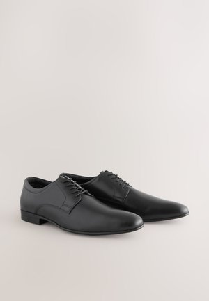 Pantofi de rochie din piele neagră cu textură netedă, vârf rotund și design cu șireturi. Au un toc jos și accente minimale de cusături.