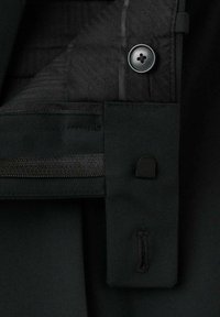 Nahaufnahme von einem schwarzen Knopf, Reißverschluss und Knopflochdetails auf strukturiertem Stoff.