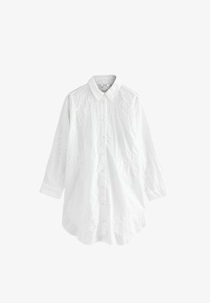 Valkoinen nappikauluspaita, pitkät hihat, etupuolella on kukka-ommeltu kuvio. Valmistettu kevyestä kankaasta, jolla on sileä pinta.