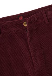 Pantaloni di velluto a coste bordeaux con righe verticali, dotati di un bottone in ottone e zip, impreziositi da una piccola etichetta sul girovita.