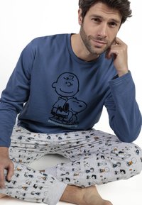 Camiseta de manga larga azul con estampado negro de Charlie Brown y Snoopy. Pantalones grises con patrones repetidos de personajes coloridos relacionados con Snoopy.