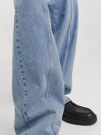 Jeans de mezclilla azul claro con un corte holgado y costuras laterales prominentes, combinados con zapatos de cuero negro con punta redonda y acentos texturizados.