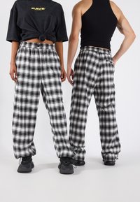 Svarta och vita rutiga byxor med elasticitet i midjan, som har en avslappnad passform och raka ben, tillsammans med svarta sneakers.