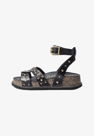 Sandalia de plataforma negra con suela de corcho, tachuelas doradas en las tiras de cuero y una correa en el tobillo con hebilla dorada.