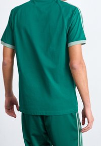 Kortärmad grön t-shirt med mjuk textur, med kontrasterande ljusgröna muddar och sidosträck, utformad för en bekväm passform.