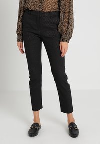 Czarne spodnie w wzory o dopasowanym kroju, skróconej długości i subtelnej fakturze. Połączone z czarnymi mokasynami z złotymi akcentami.