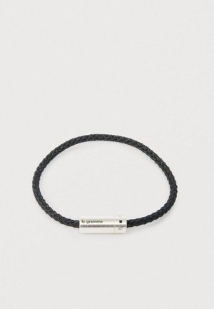 Czarny pleciony skórzany bransoletka z cylindrycznym zapięciem ze srebra, na którym wygrawerowane jest "le gramme" oraz "7g" na jasnym tle.