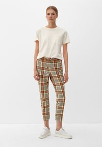 T-shirt crème en coton à manches courtes avec une poche poitrine, associé à un pantalon à carreaux aux tons orange, marron et crème. Baskets blanches.