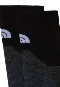 Calcetines negros y grises con textura acanalada, que presentan un diseño geométrico. Detalle notable de un logotipo en azul claro cerca del puño.