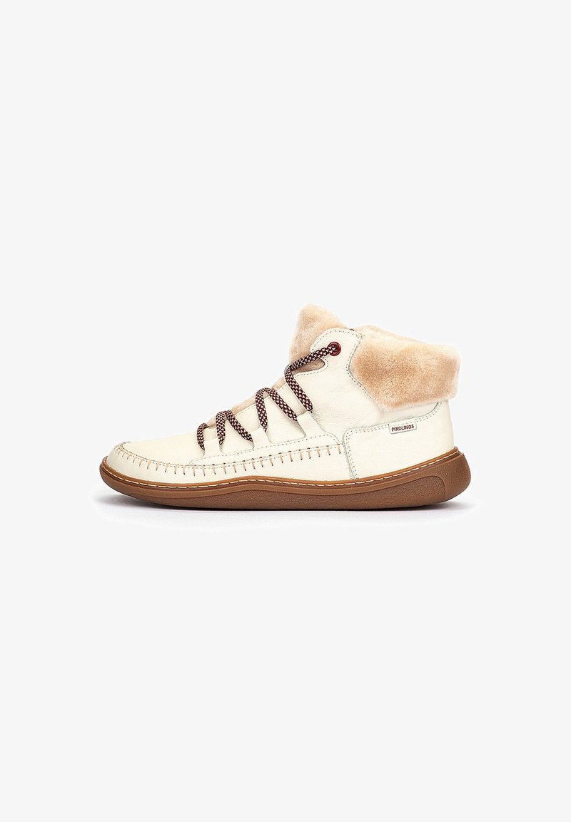 Zapatillas altas de cuero crema con un suave cuello de piel, suela marrón y cordones marrones. Presentan costuras decorativas a lo largo de los lados.