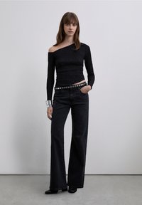 Musta, ribbineulottu pitkähihainen paita, jossa yksi paljas olkapää, yhdistetty korkeavyötäröisiin mustiin leveälahkeisiin farkkuihin ja niitillä koristeltuun hopeiseen vyöhön.