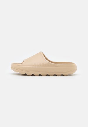 Sabot beige à enfiler avec surface texturée, semelle épaisse et semelle rainurée pour une bonne adhérence, présenté de profil gauche sur fond blanc.