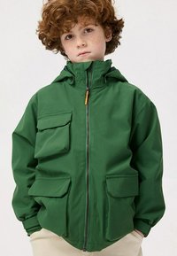Groene jas met een capuchon, voorzien van een volledige ritssluiting, vier zakken en een soepele textuur. Ontworpen in een praktische, oversized vorm.