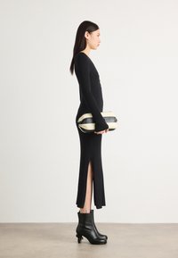 Lang svart ribbet kjole med sideslitt, parret med svarte ankelstøvletter med hæl. Modellen holder en stripet svart og kremfarget clutch.