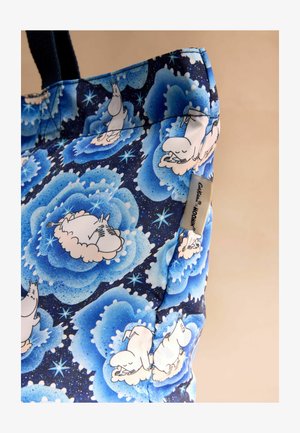 Kottitasku on valmistatud sinisest kangast, millel on lillemuster ja koomiksitegelased tumeda tausta peal. Ülaservas on õmmeldud silt brändingu jaoks.