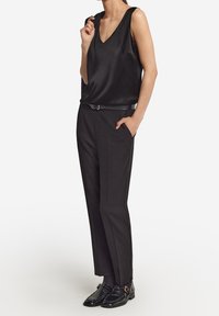 Top sans manches en satin noir avec un col en V, associé à un pantalon noir ajusté et des chaussures noires brillantes avec un détail de boucle.