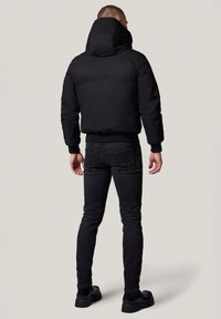 Czarna kurtka puchowa z wysokim kołnierzem i kapturem, zestawiona z czarnymi dopasowanymi dżinsami i czarnymi bootami. Matowa tekstura, prosty design, bez widocznych wzorów.