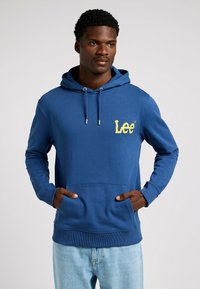 Sudadera azul de algodón con un bolsillo canguro en el frente, capucha ajustable con cordón y un logo amarillo en el pecho izquierdo.
