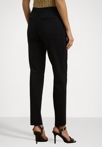 Černé přizpůsobené kalhoty s hladkým povrchem, slim fit, bočními kapsami a středním pasem, doplněné černými sandály na vysokém podpatku.