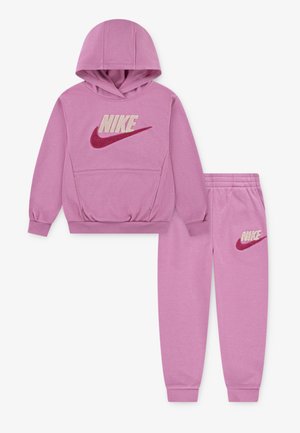 Rosa Kapuzenpullover und Jogginghose aus weichem Stoff. Der Kapuzenpullover hat ein großes, flauschiges Nike-Logo; die Hose hat ein kleineres Logo auf dem Oberschenkel.